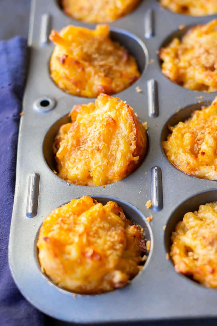 Close up of baked Mac and Cheese cups popped up out of the muffin pan with a blue towel showing slightly on the side