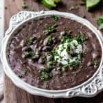 Close up of Black bean and lime soup in a white bowl on a wood board with lime slices and cilantro