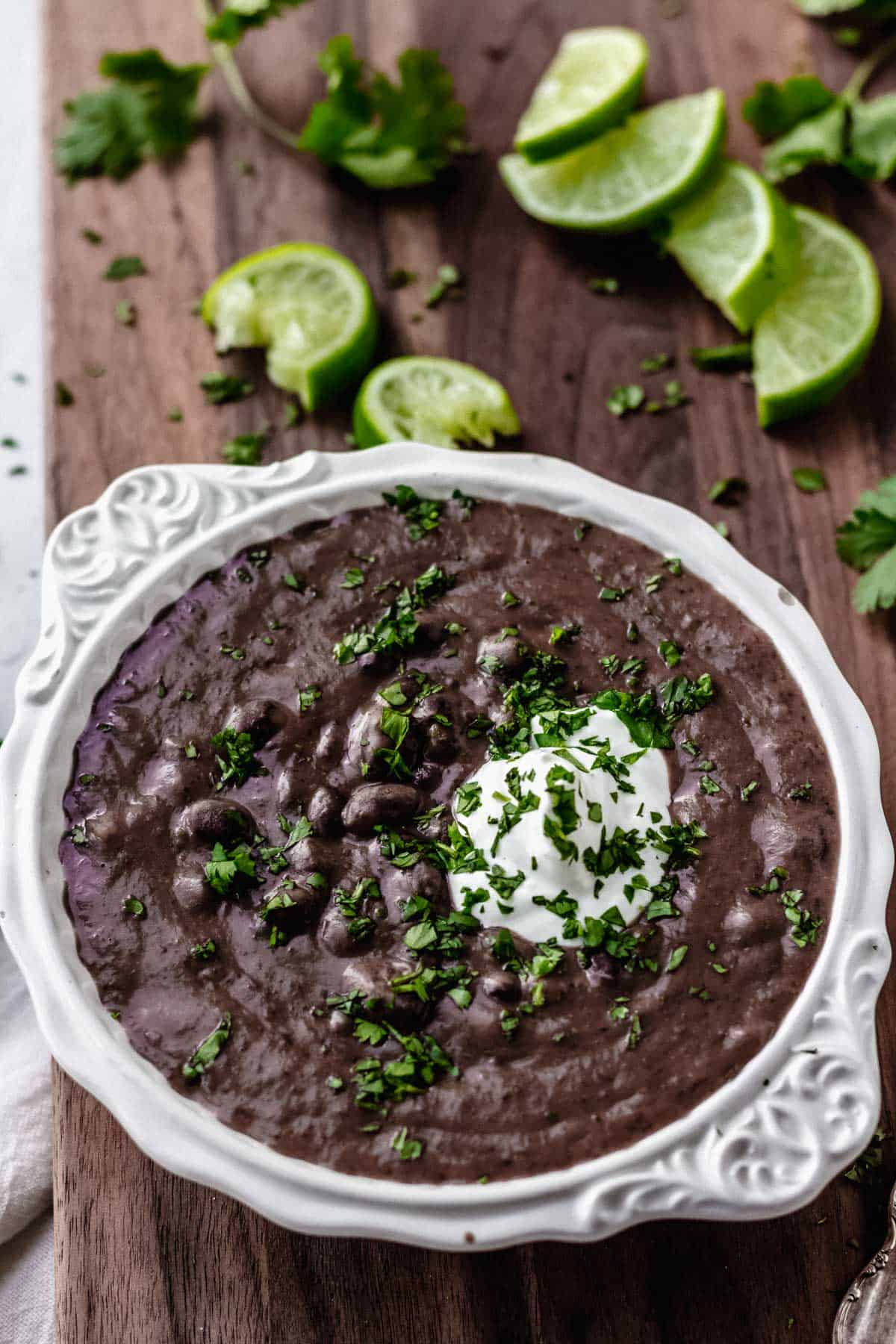 Black bean and lime soup in a white bowl on a wood board with lime slices and cilantro