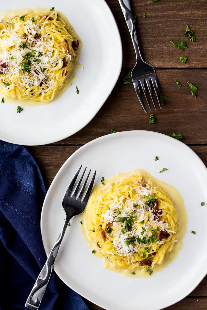 Overhead View of Two Plates of Spaghetti Squash Carbonara on a wood background with 2 forks and a dark blue napkin
