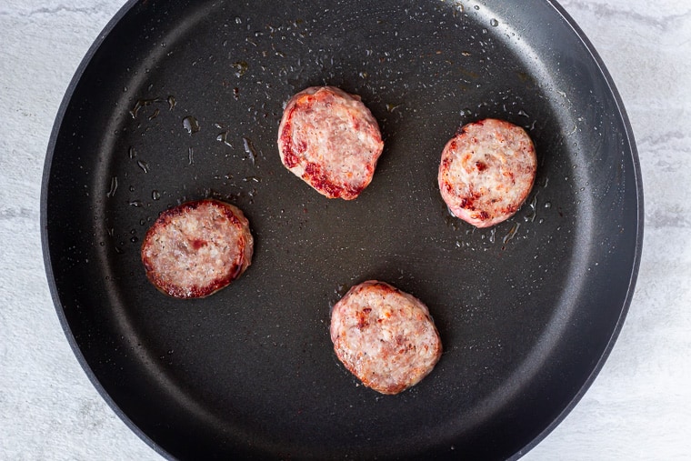 4 sausage patties cooking in a black skillet over a white background