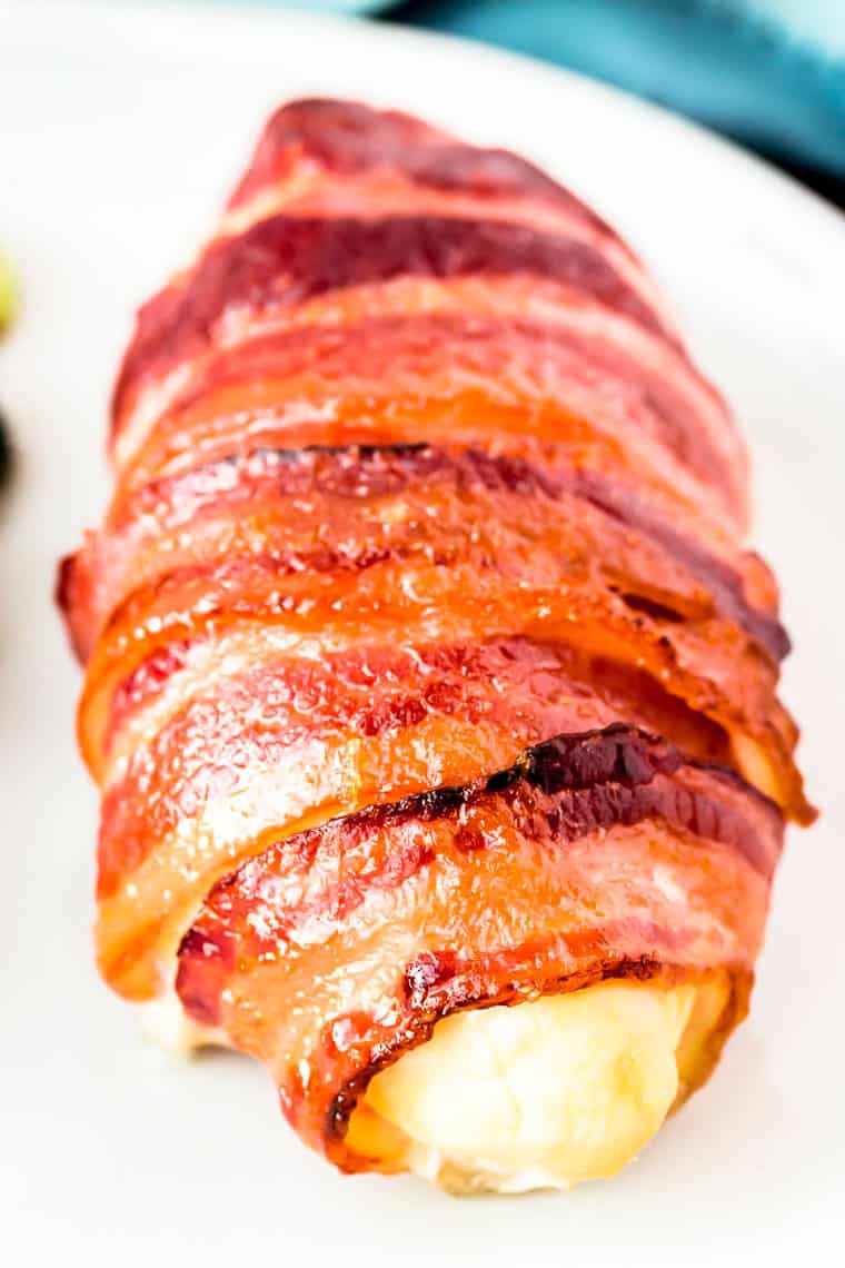 Close up of a single bacon wrapped chicken breast on a white plate