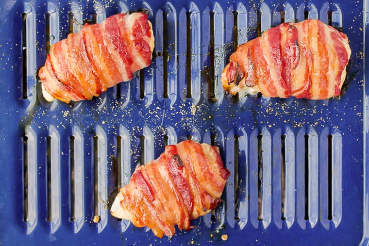 3 baked bacon wrapped chicken breasts on a blue broiler pan