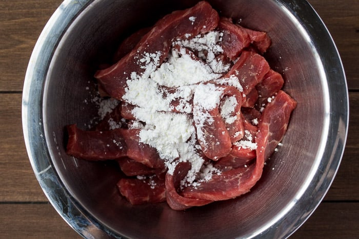 Beef strips and Corn Starch in a silver Bowl over a wood background