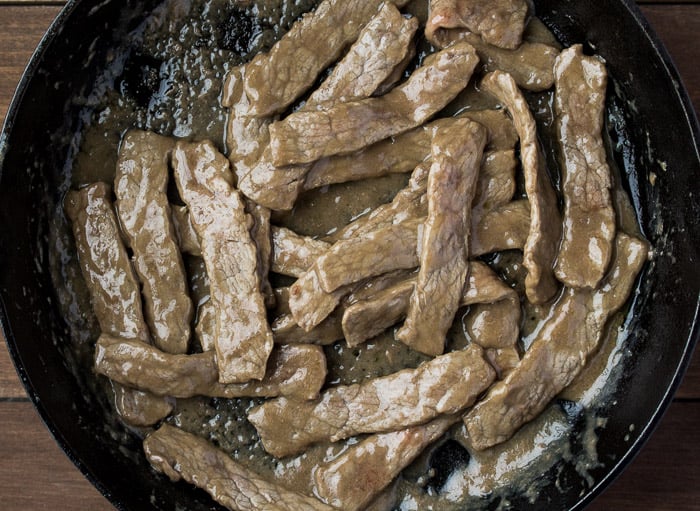 Beef Strips Cooking in a black skillet over a wood background