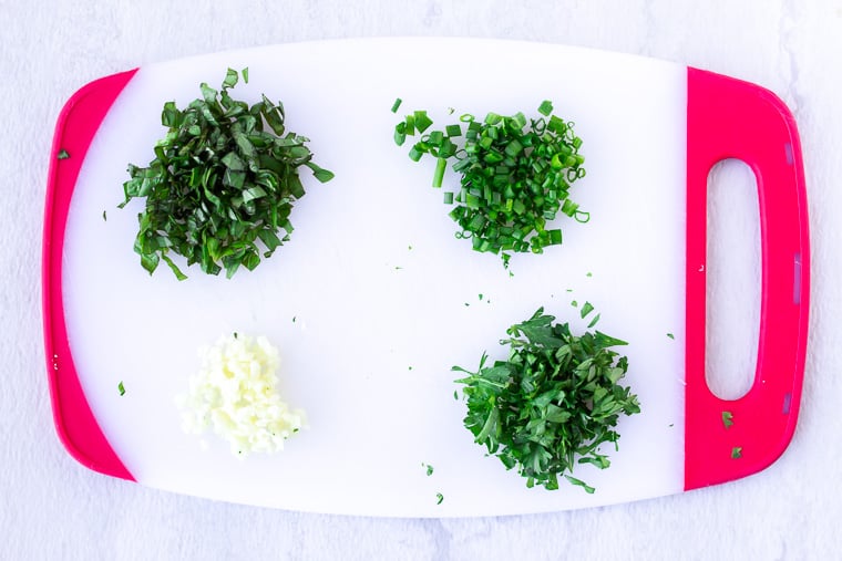 Minced herbs and garlic on a red and white cutting board