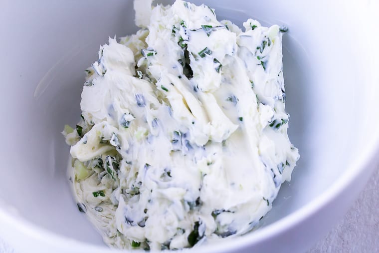 Cream cheese and herbs blended together in a white bowl