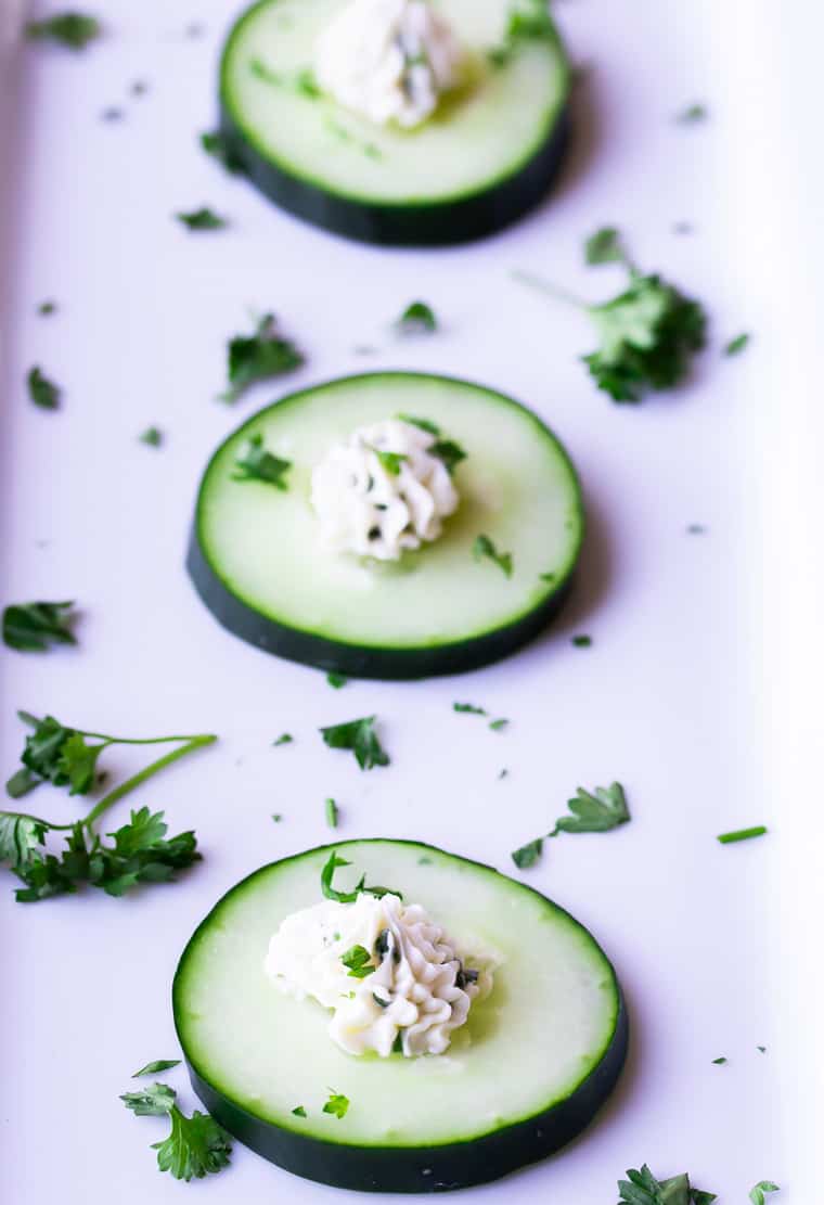 3 cucumber slices topped with herbed cream cheese on a white serving tray