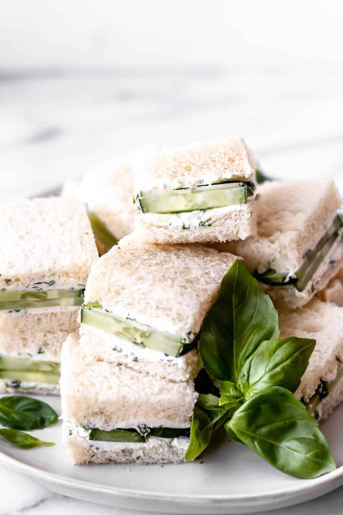 Cucumber tea sandwiches stacked on a white plate.