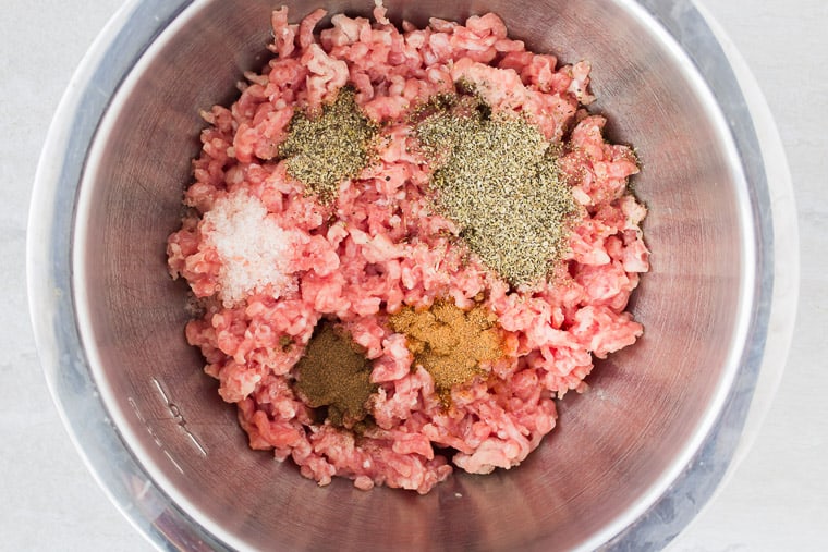 Ground pork in a silver bowl with different spices on top before combining