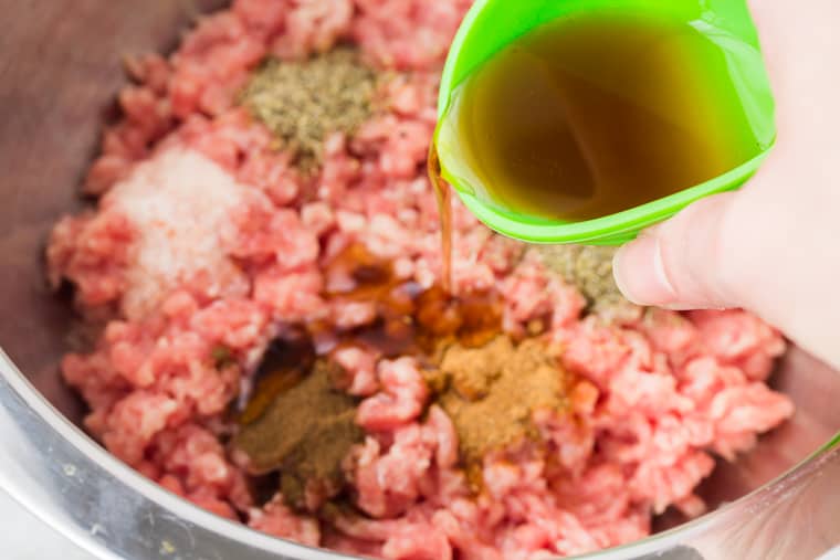 Maple syrup being poured out of a green bowl into a silver bowl with ground pork and spices