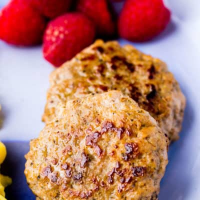 Close up of 2 Homemade Breakfast Sausage patties on a blue plate with scrambled eggs and fresh raspberries