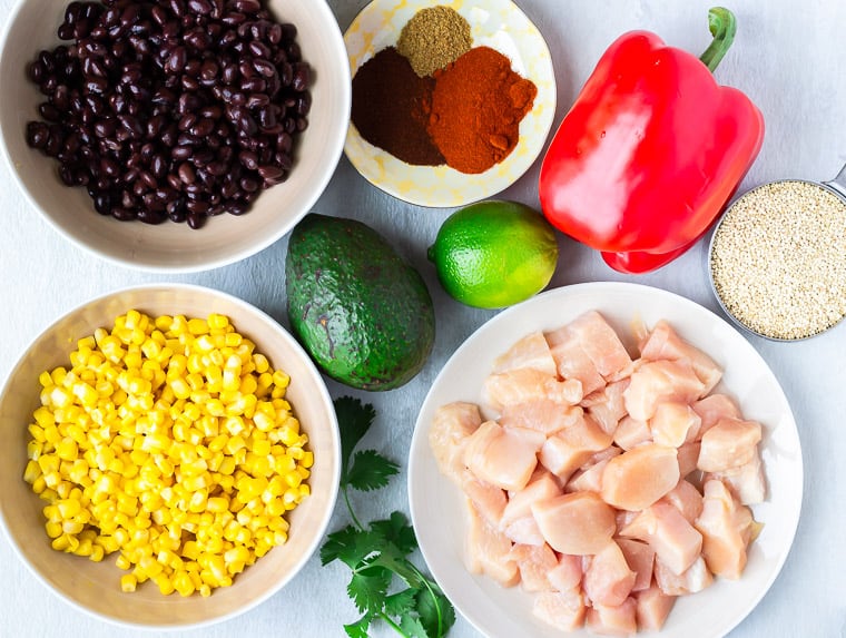 Ingredients needed to make southwestern chicken and quinoa in bowls or sitting on a white background