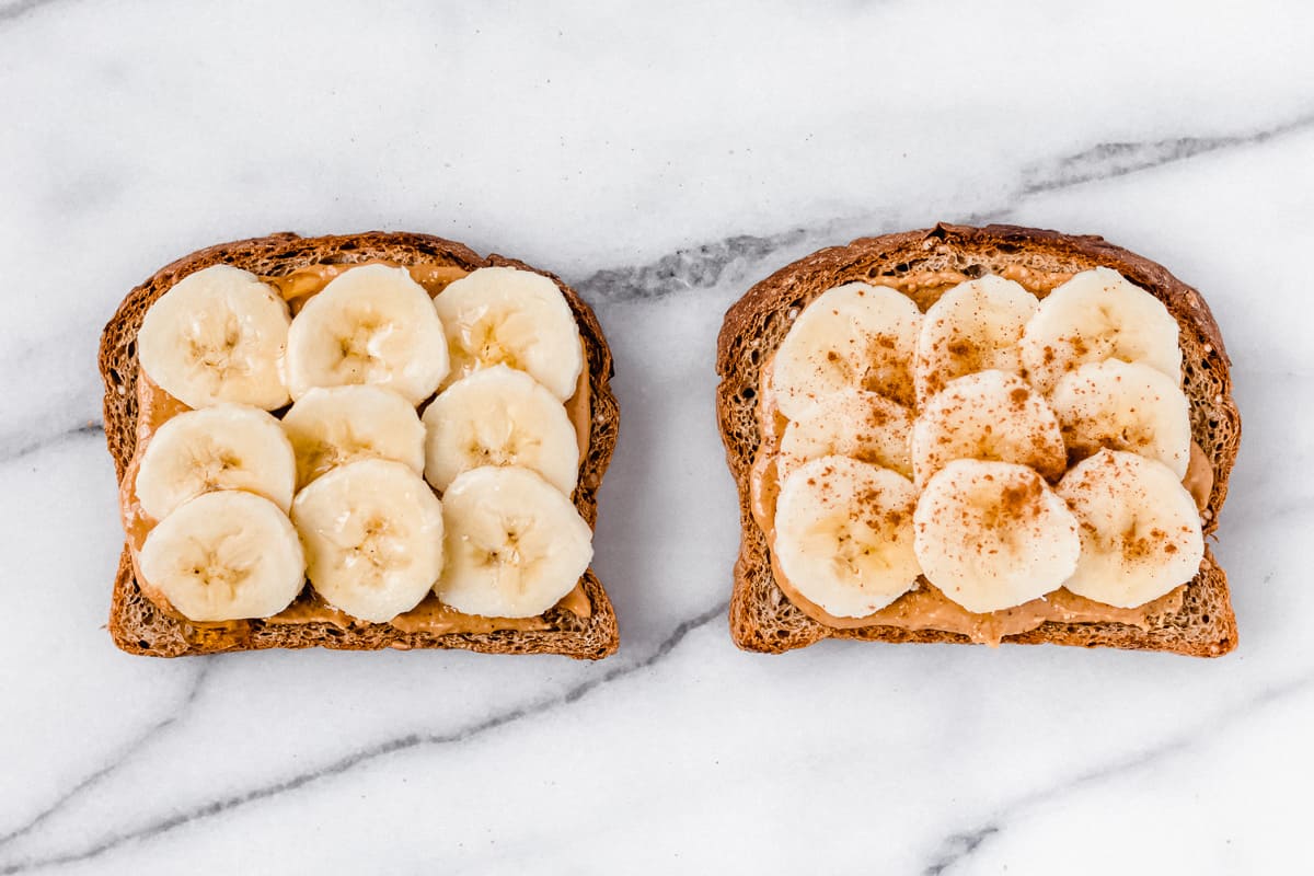2 slices of toast with banana slices, peanut butter, honey and cinnamon on a marble background
