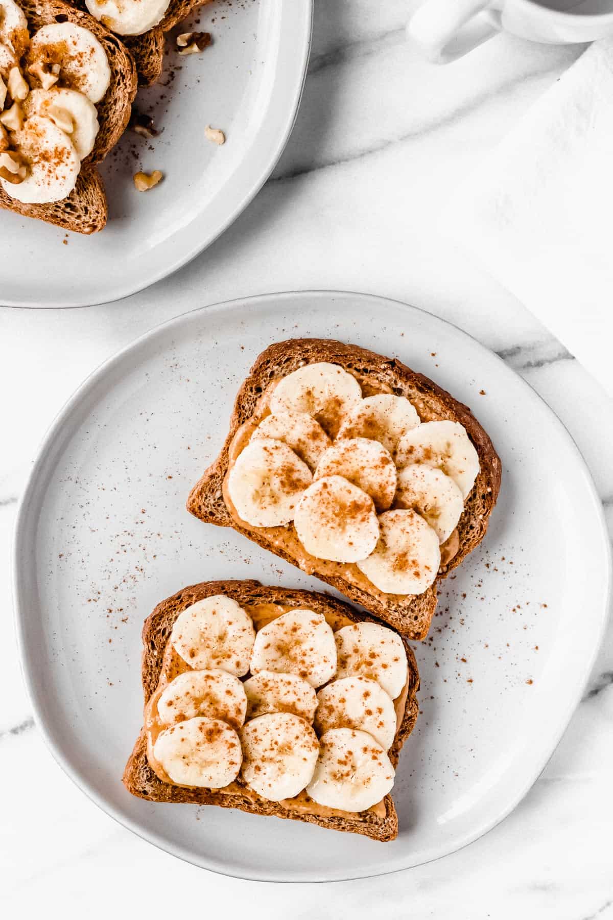 Overhead of banana toast with peanut butter, cinnamon and honey on a white plate