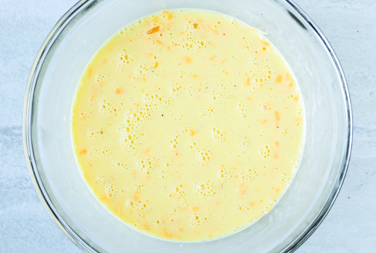 Bowl of egg batter with cheese in a glass bowl over a white background