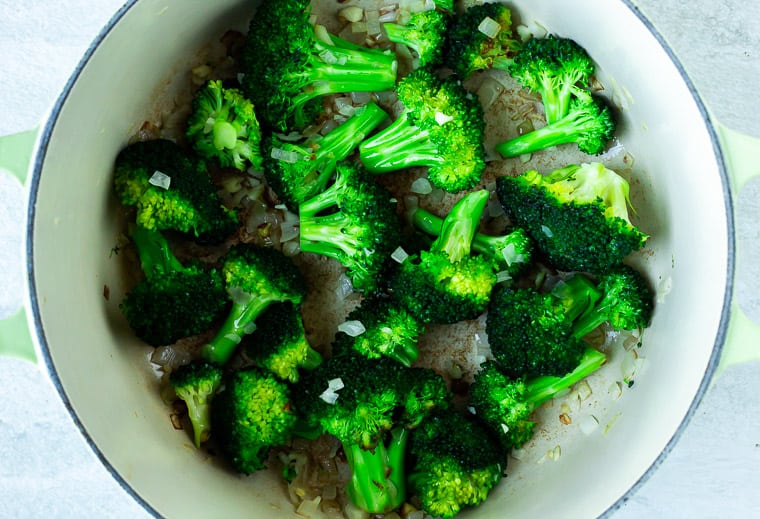 Broccoli, shallot, and garlic in a Dutch oven over a white background