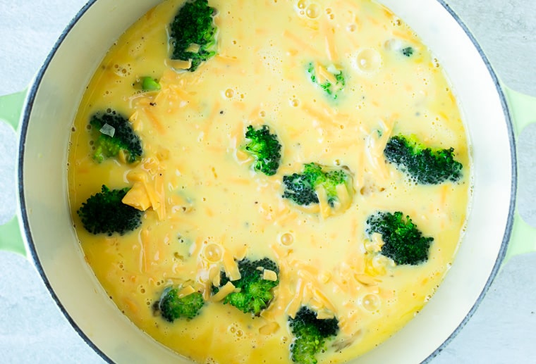 Egg batter and broccoli in a Dutch oven over a white background