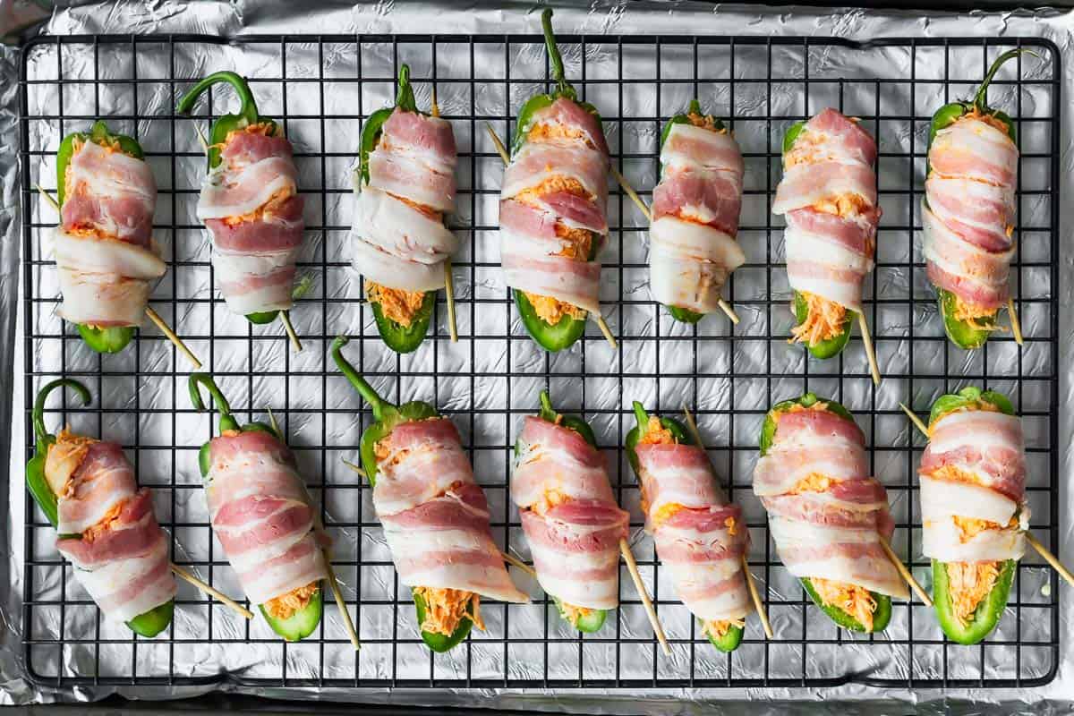 Buffalo chicken jalapeno poppers wrapped in bacon on a baking rack before cooking