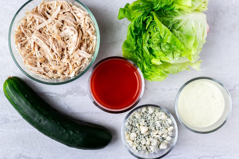 Ingredients needed to make Buffalo Chicken Lettuce Wraps in glass bowls on a which background