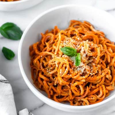 Carrot noodles with pesto in a white bowl with basil leaves around it.