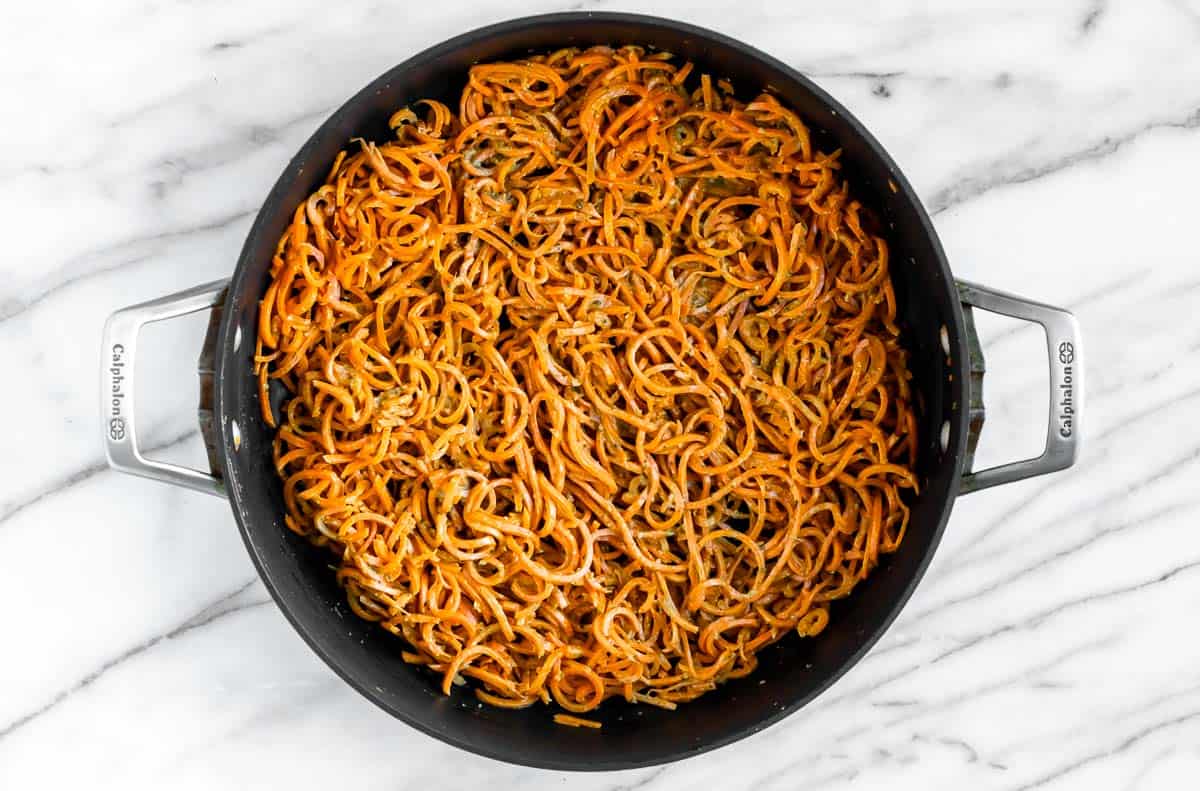 Carrot noodles mixed with pesto in a large skillet.