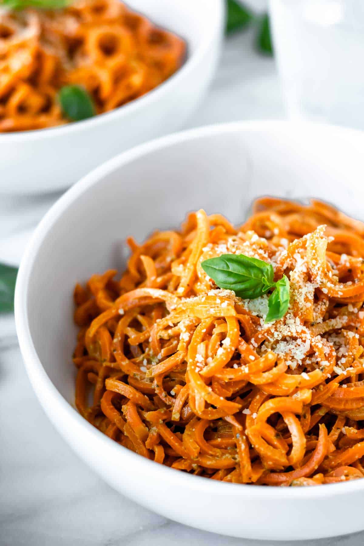 Close up of carrot noodles with pesto in a white bowl.