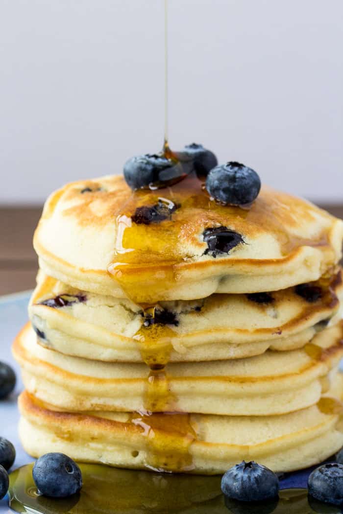 A Stack of Fluffy Blueberry Pancakes with Syrup Being Poured on Top