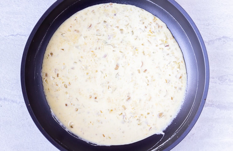 White cheese sauce cooking in a black skillet over a white background