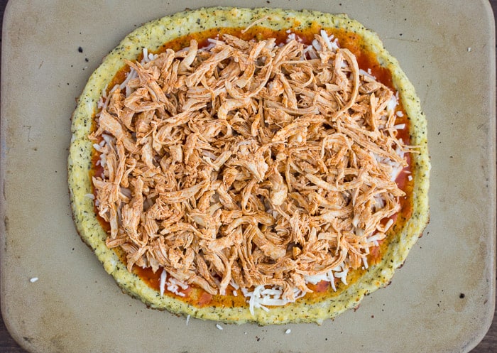 Cauliflower crust Pizza topped with Buffalo Chicken on a pizza stone prior to baking