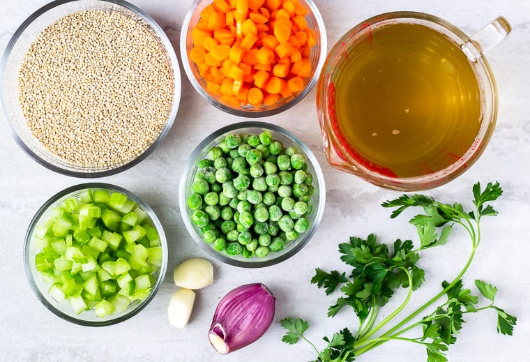Ingredients needed to make quinoa pilaf in glass bowls on a white background