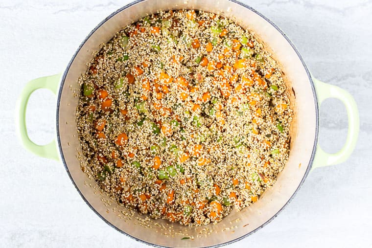 Quinoa and vegetables cooking in a light green dutch oven over a white background
