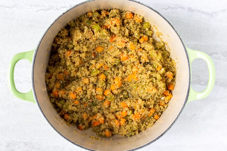 Cooked quinoa and vegetables in a light green dutch oven over a white background