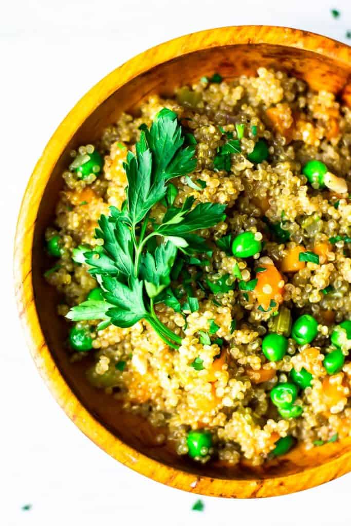 close up of quinoa pilaf in an orange wood bowl over a white background