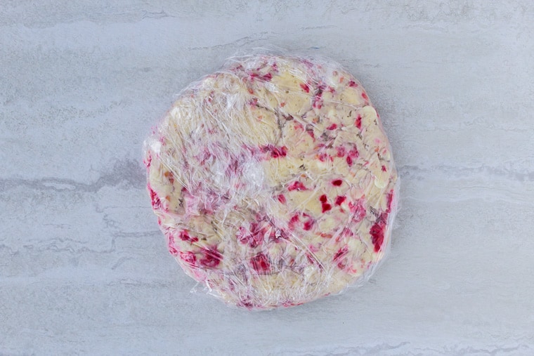 White Chocolate Raspberry Scones dough wrapped in plastic wrap for freezing on a white backdrop
