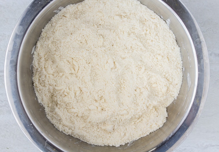 Course crumbles of flour and butter for scones in a silver mixing bowl on a white backdrop