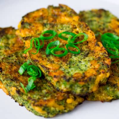 Broccoli Cheddar Cauliflower Hash Browns Stacked on a White Plate with Sliced Green Onions