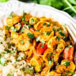 Close up of Coconut Curry Shrimp in a white bowl with a lime and cilantro blurred in the background