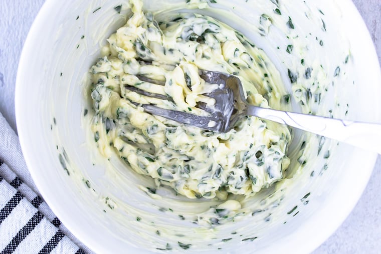 butter, herbs and garlic mashed together with a fork in a white bowl over a white background
