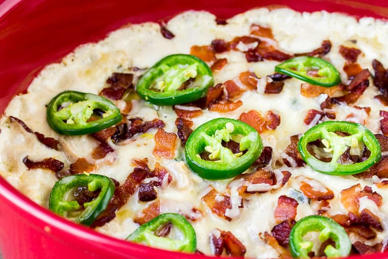 A Close up of Jalapeno Popper Casserole in a Red Casserole Dish topped with slices of jalapeno peppers