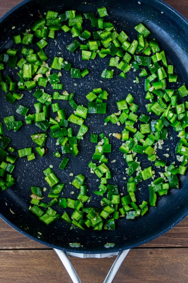 Overhead View of Diced Jalapeno Peppers Cooked in a Black Skillet on a Wood Background
