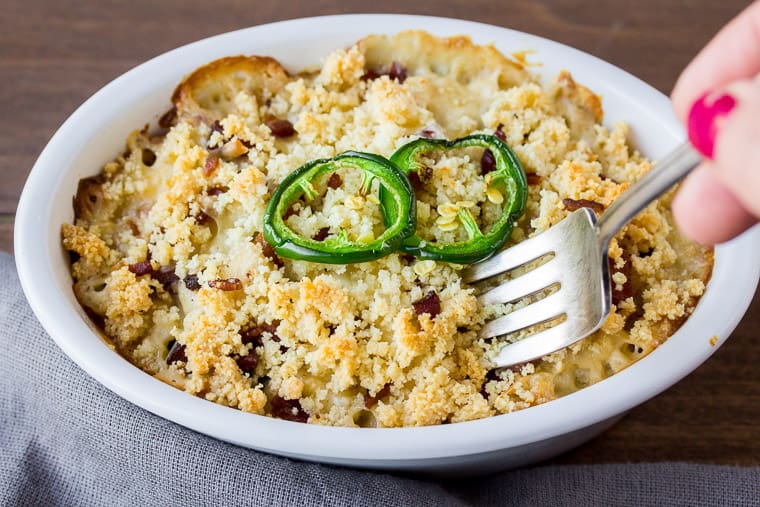 Jalapeno Popper Cauliflower Casserole with Almond Flour Breadcrumbs, a fork being put in it with a gray napkin on a wood background
