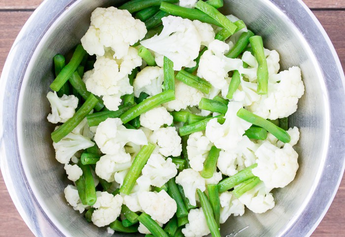 Cut Green Beans and Cauliflower in a Large silver Bowl over a wood background