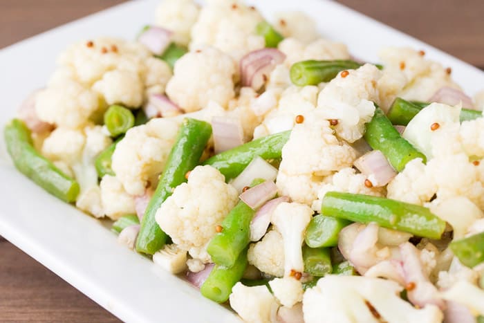 Close up of Green Bean Cauliflower Salad on a White Serving Tray over a wood background