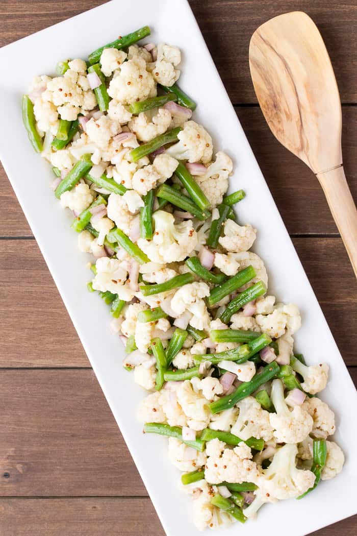 Green Bean Cauliflower Salad on a White Rectangular Tray with a Wooden Spoon on a wood background