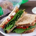 A Roasted Red Pepper Spinach Sandwich Cut in Half on a White Plate