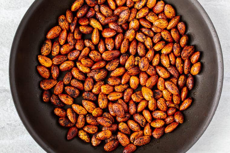 Almonds and chipotle chili powder cooking in a black skillet over a white background