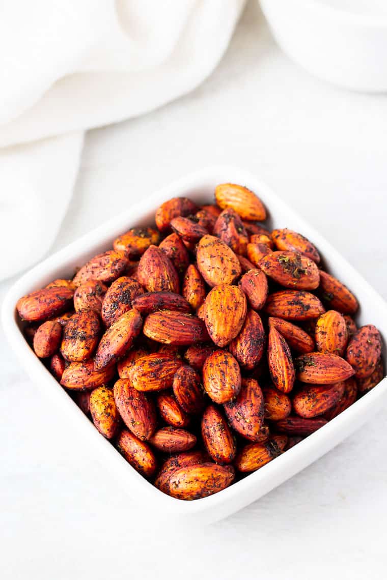 Chipotle Lime Almonds in a square bowl on a white background with a white towel and a white bowl in the background