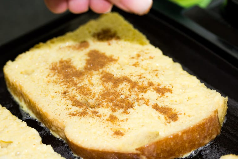 Close up of a piece of French Toast on a Griddle with Cinnamon Being Sprinkled on Top