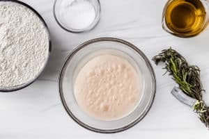 Yeast proofing in a glass bowl over a white background with other ingredients around it
